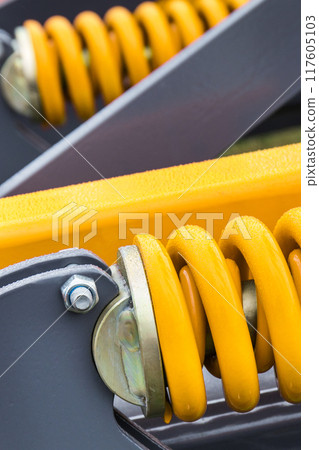 Yellow hard spring made of steel. Part of big industrial or agricultural machine 117605103