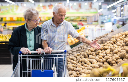 Mature spouses chooses potato in vegetable section of supermarket Mature spouses chooses potato in vegetable section of supermarket 117605637