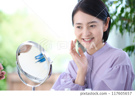 Middle-aged woman doing skin care in the living room Middle-aged woman doing skin care in the living room 117605657