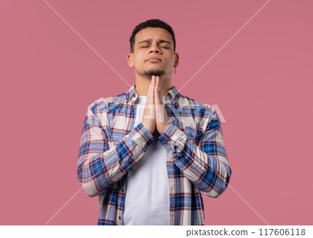Young multiracial man praying with crossed fingers on pink. Guy begs someone 117606118
