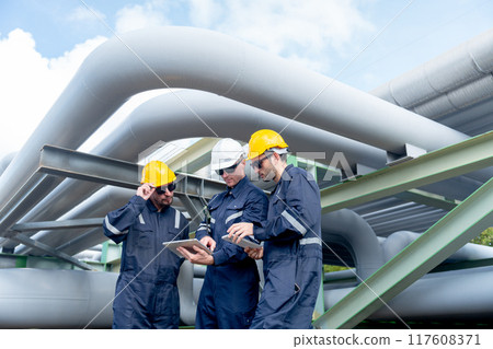 Close up group of engineer or factory technician worker team stand near and under petrochemical gas pipeline and use tablet to discuss about their work in workplace. Close up group of engineer or factory technician worker team stand near and under petrochemical gas pipeline and use tablet to discuss about their work in workplace. 117608371