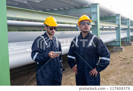 Close up two engineer or factory technician workers stand beside petrochemical gas pipeline and use tablet to discuss about their work. 117608379