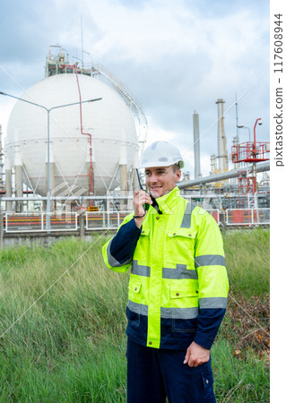 Vertical image of engineer or technician worker stand with hold walkie-talkie in front of petrochemical tank with day light. 117608944