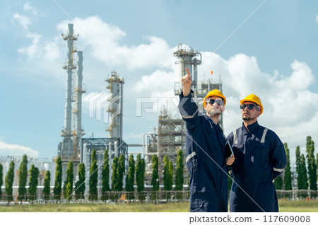 Two factory engineer or technician workers with one hold tablet and point forward look like explain work to coworker and stand in front of refining petrochemical factory with day light. Two factory engineer or technician workers with one hold tablet and point forward look like explain work to coworker and stand in front of refining petrochemical factory with day light. 117609008