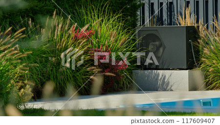 Outdoor heat pump unit installed near a backyard pool, surrounded by blooming plants. 117609407