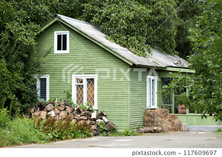 One-storey green wood house with a roof is surrounded by greenery in summer. Old traditional wooden house. Green vintage country house One-storey green wood house with a roof is surrounded by greenery in summer. Old traditional wooden house. Green vintage country house 117609697