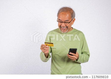 Portrait Asian smiling old man is holding a credit card and a cell phone. He is likely checking his bank account balance or making a purchase studio shot isolated on white background 117609810