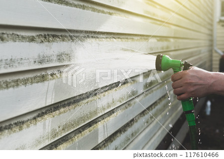 Cleaning algae and mold from vinyl siding of house with pressure spray jet 117610466