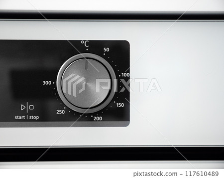 Woman adjusting modern white oven in kitchen.  Female hand pushing and turning knobs on oven control panel 117610489