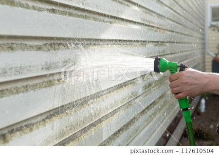 Cleaning algae and mold from vinyl siding of house with pressure spray jet 117610504