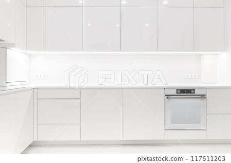 Front view of a modern luxury trendy snow white kitchen with many cabinets Front view of a modern luxury trendy snow white kitchen with many cabinets 117611203