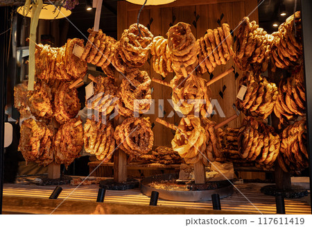 Tasty handmade pretzels with different toppings hanging for sale in marketplace, delicious bakery at street cafe Tasty handmade pretzels with different toppings hanging for sale in marketplace, delicious bakery at street cafe 117611419