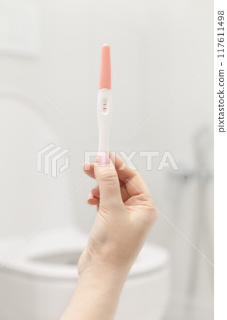 Holding positive pregnancy test in rest room 117611498