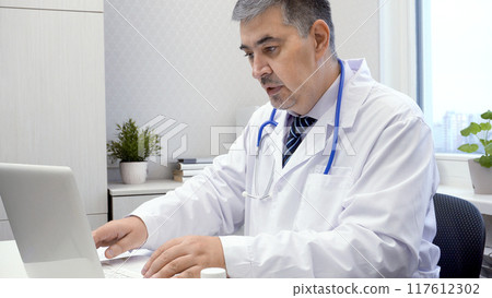 Male Doctor Working on Computer in Office Male Doctor Working on Computer in Office 117612302