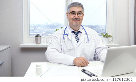 Smiling male doctor sitting at the desk Smiling male doctor sitting at the desk 117612305