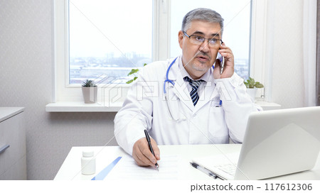 Male Doctor Talking on the Phone at His Desk 117612306
