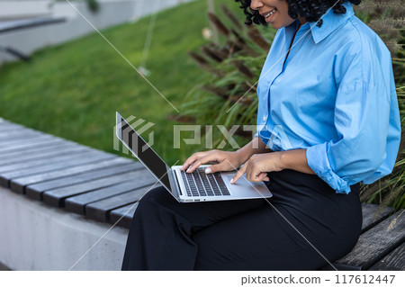 Close up of woman in blue shirt working on laptop 117612447