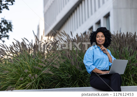 Brunette woman with laptop sitting on a bench and working 117612453