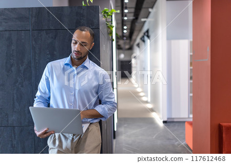 Confident businessman in office hall with laptop 117612468