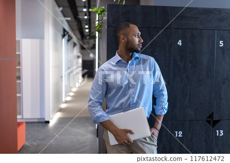 African American businessman holding laptop in office hall 117612472
