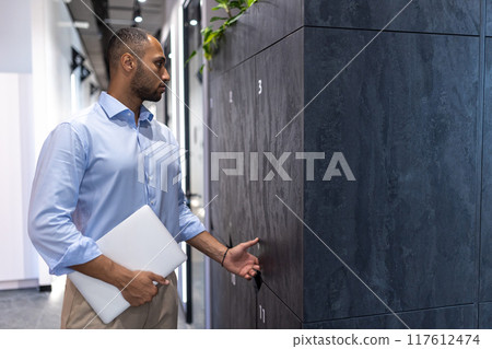 Confident businessman in office hall with laptop Confident businessman in office hall with laptop 117612474