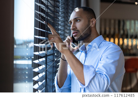 Black guy next to window talking on smartphone in cafe interior 117612485