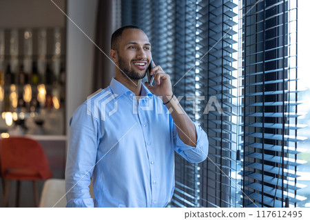 Black guy next to window talking on smartphone in cafe interior 117612495