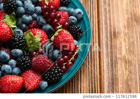 Mix of ripe colorful berries in bowl photography . Blueberry , strawberry , raspberry , blackberry and red currant . Top view 117612598
