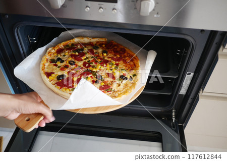 When baking a homemade pizza in the oven, ensure safety by wearing a protective glove on your hand When baking a homemade pizza in the oven, ensure safety by wearing a protective glove on your hand 117612844