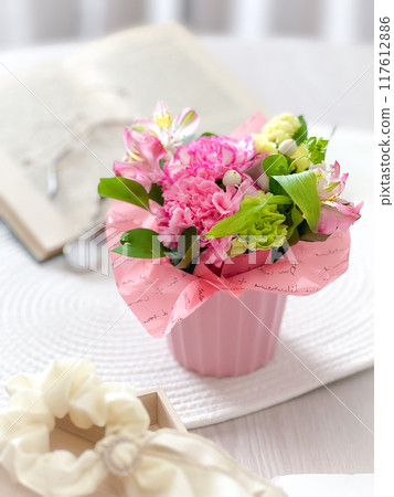 A soft and gentle flower arrangement with a bouquet of pink flowers, mainly carnations, placed on a table. 117612886