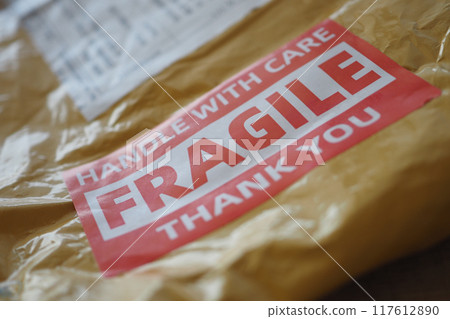 A cardboard box marked with a caution label for fragile goods handling during shipping A cardboard box marked with a caution label for fragile goods handling during shipping 117612890