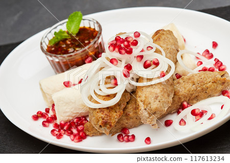 Traditional grilled kebab with pomegranate, onions, spicy sauce for flavorful culinary experience Traditional grilled kebab with pomegranate, onions, spicy sauce for flavorful culinary experience 117613234