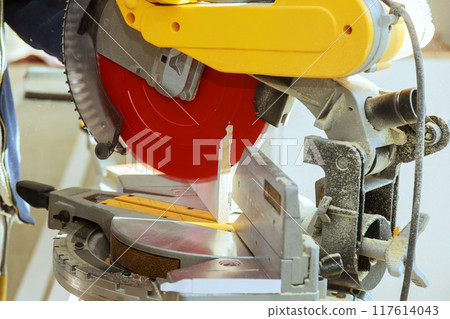 Professional carpenter cutting wooden molding trim with electric circular saw at sawmill 117614043