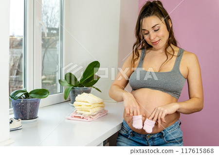 A radiant pregnant woman tenderly cradles baby socks near her belly 117615868