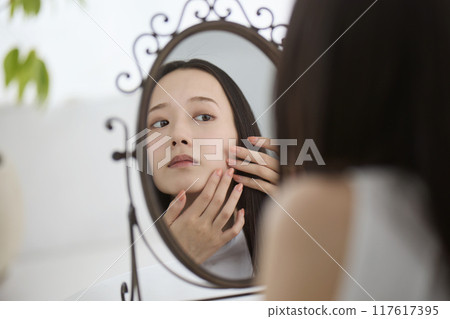 A woman checking her skin in the mirror A woman checking her skin in the mirror 117617395
