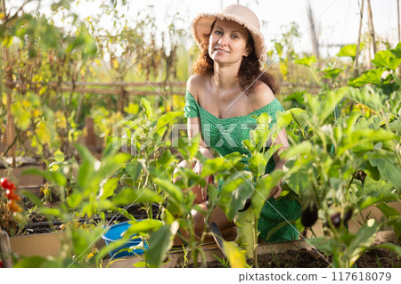Slender woman in green dress and straw hat poses in her garden, in the backyard of country house Slender woman in green dress and straw hat poses in her garden, in the backyard of country house 117618079