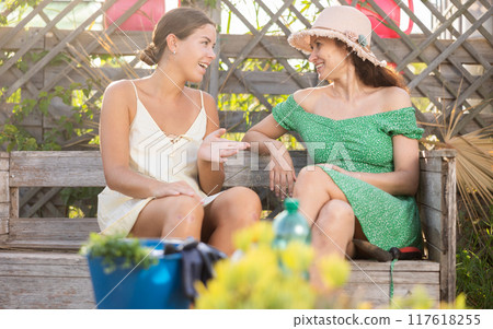 Conversation between two adult friends who are sitting on bench in ourtyard of country house Conversation between two adult friends who are sitting on bench in ourtyard of country house 117618255