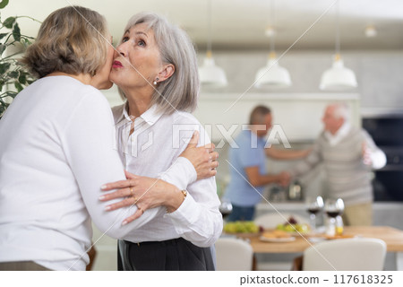 After chatting and gatherings, two mature women friends hug and kiss goodbye. 117618325