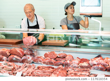 Adult man and young woman sellers lay out and weigh beef in butcher shop Adult man and young woman sellers lay out and weigh beef in butcher shop 117618354