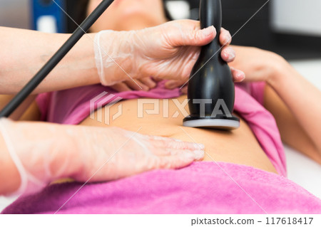 Cosmetology doctor makes a young female client a vacuum massage of the abdomen Cosmetology doctor makes a young female client a vacuum massage of the abdomen 117618417