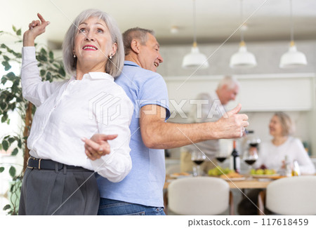 Senior man and woman doing couple dancing with their backs to each other during house party. 117618459