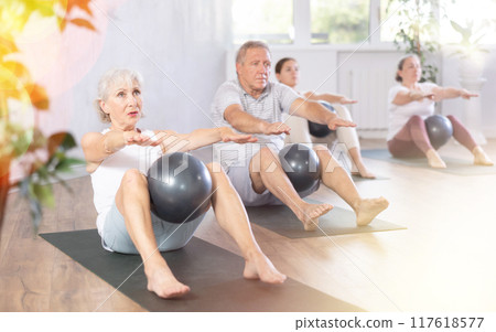 Mature people with young coach sit on karemat, pulled leg to themselves and clamped softball in knee 117618577