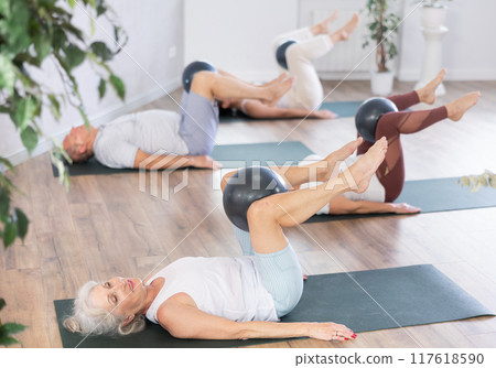 Mature woman doing exercises with pilates ball during group training at gym indoor Mature woman doing exercises with pilates ball during group training at gym indoor 117618590