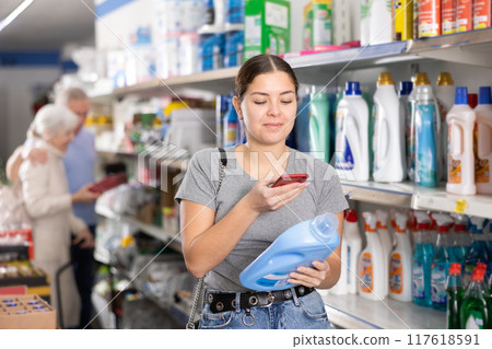 Young female customer scanning barcode on plastic bottle of household detergent with smartphone while shopping in supermarket, paying for item using mobile app Young female customer scanning barcode on plastic bottle of household detergent with smartphone while shopping in supermarket, paying for item using mobile app 117618591