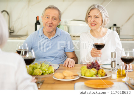 Mature married couple with female friend are sitting at table, enjoying food and wine, chatting. 117618623