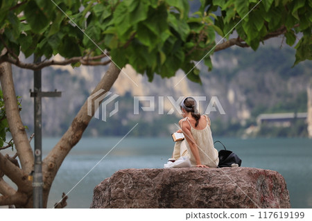 A Serene Woman Sitting Peacefully by the Tranquil Water in the Heart of Natures Beauty 117619199