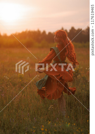 A shepherdess woman with red hair and a green dress sits in a field of flowers. 117619465