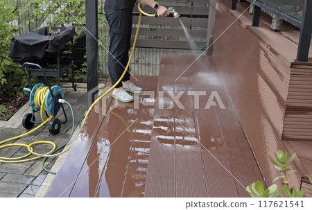 Anonymous cleaning, hose washing deck in summer. Structures in backyard. Clean and orderly. Anonymous cleaning, hose washing deck in summer. Structures in backyard. Clean and orderly. 117621541