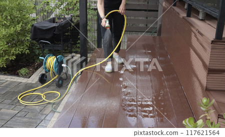 Anonymous cleaning, hose washing deck in summer. Structures in backyard. Clean and orderly.  117621564