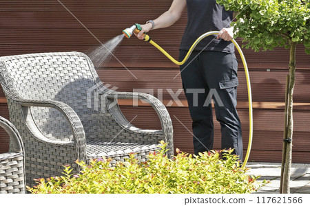 Anonymous cleaning, hose water washing wicker furniture from summer. Structures in backyard. Cleanliness and order.  117621566